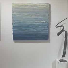 A video of a blue, beige, lavender and light yellow textured abstract painting by Teodora Guererra hangs on a white wall.