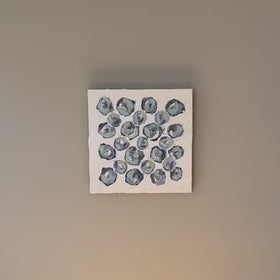 A video of a very textured abstract painting with white background and circle type abstract flowers in blue, teal, green, plum and white hanging on a grey wall.