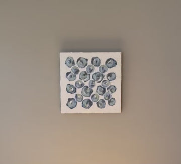 A video of a very textured abstract painting with white background and circle type abstract flowers in blue, teal, green, plum and white hanging on a grey wall.