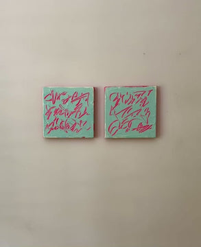 A video of two square abstract text based paintings hanging side by side on a textured off-white wall. 