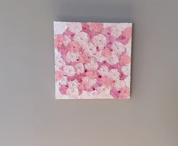 A video of a very textured abstract painting with white background and circle type abstract flowers in pink and white hanging on a grey wall.