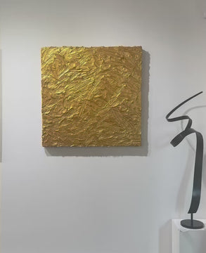 A video of a metallic gold thick textured painting on a white wall in natural light by Teodora Guererra.