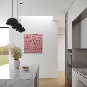 A coral pink text based painting with navy abstract calligraphic lines hangs on a white wall in a modern kitchen with white cabinets, a marble island, and green pendant lights.