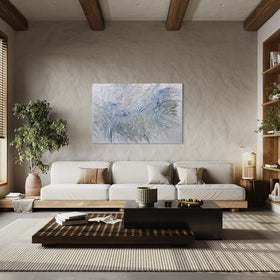 Original abstract painting with very textured blue and white brushstrokes hanging on a white sunlit wall in a living room with a sofa, coffee table, and decorative elements.