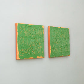 Two square abstract text based paintings with thick green paint and tangerine gestural lines, mounted on a light gray wall.