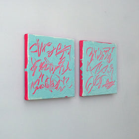 Two square abstract text based paintings with turquoise backgrounds and pink scribbled lines, displayed side by side on a light gray wall, side view.