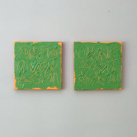 Two square abstract paintings side by side on a light gray wall. Each painting features textured green paint with tangerine texted abstract brushstrokes and a thin orange border.