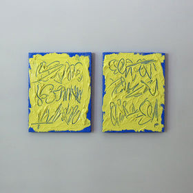 Two abstract text based painting featuring a thick, yellow-green impasto texture with blue abstract scribbled lines and a bright blue background hang on a grey wall.