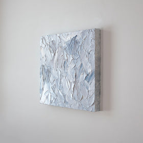 A painting is shown hanging on the wall at an angle. Its surface is decorated with white, blue and grey paint in a thick impasto. Wired and ready to hang.