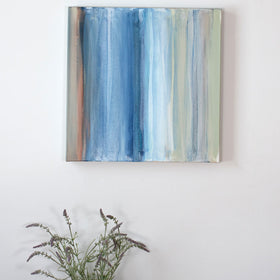 An original painting painted in tan, blue, white, and green streaks hangs above a shelf decorated with lavender and seashells. Wired and ready to hang.